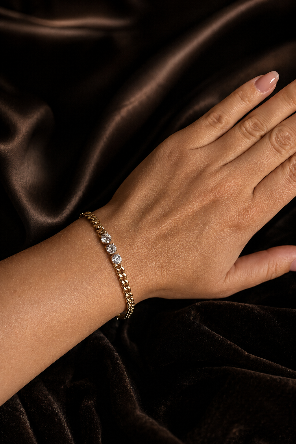 18k gold-plated chain bracelet with three zircons on the hand in a dark fabric background