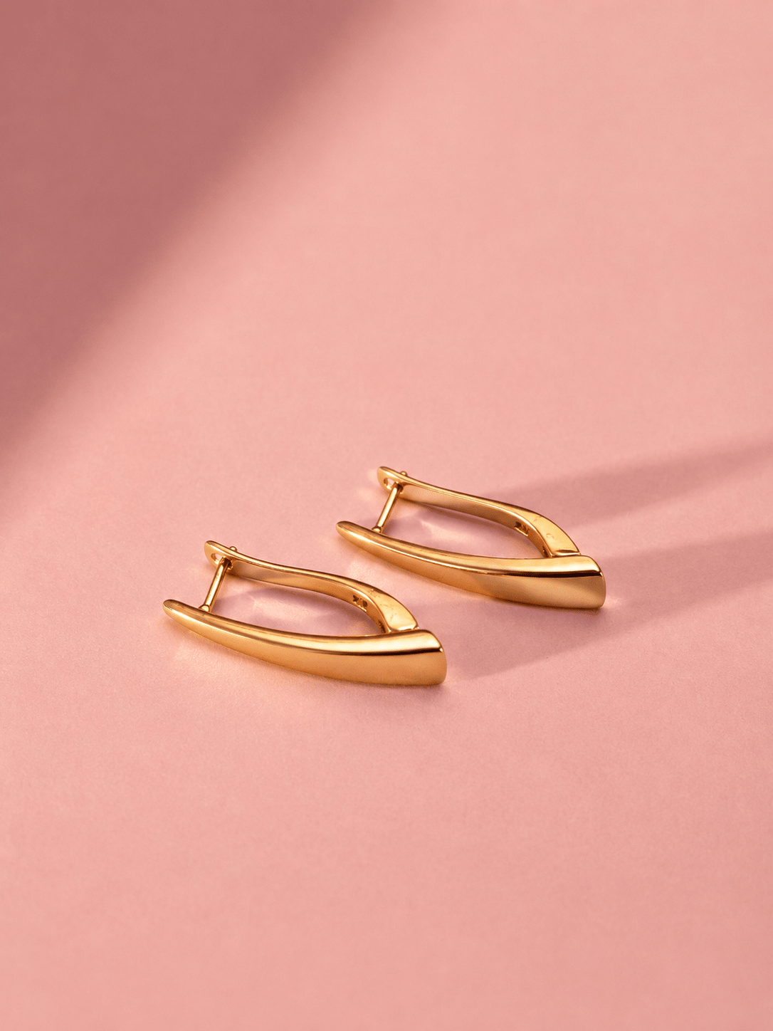 A pair of 18k gold-plated elongated earrings on a pink background