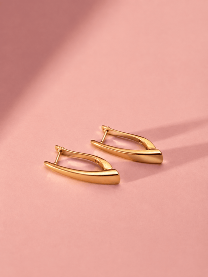 A pair of 18k gold-plated elongated earrings on a pink background