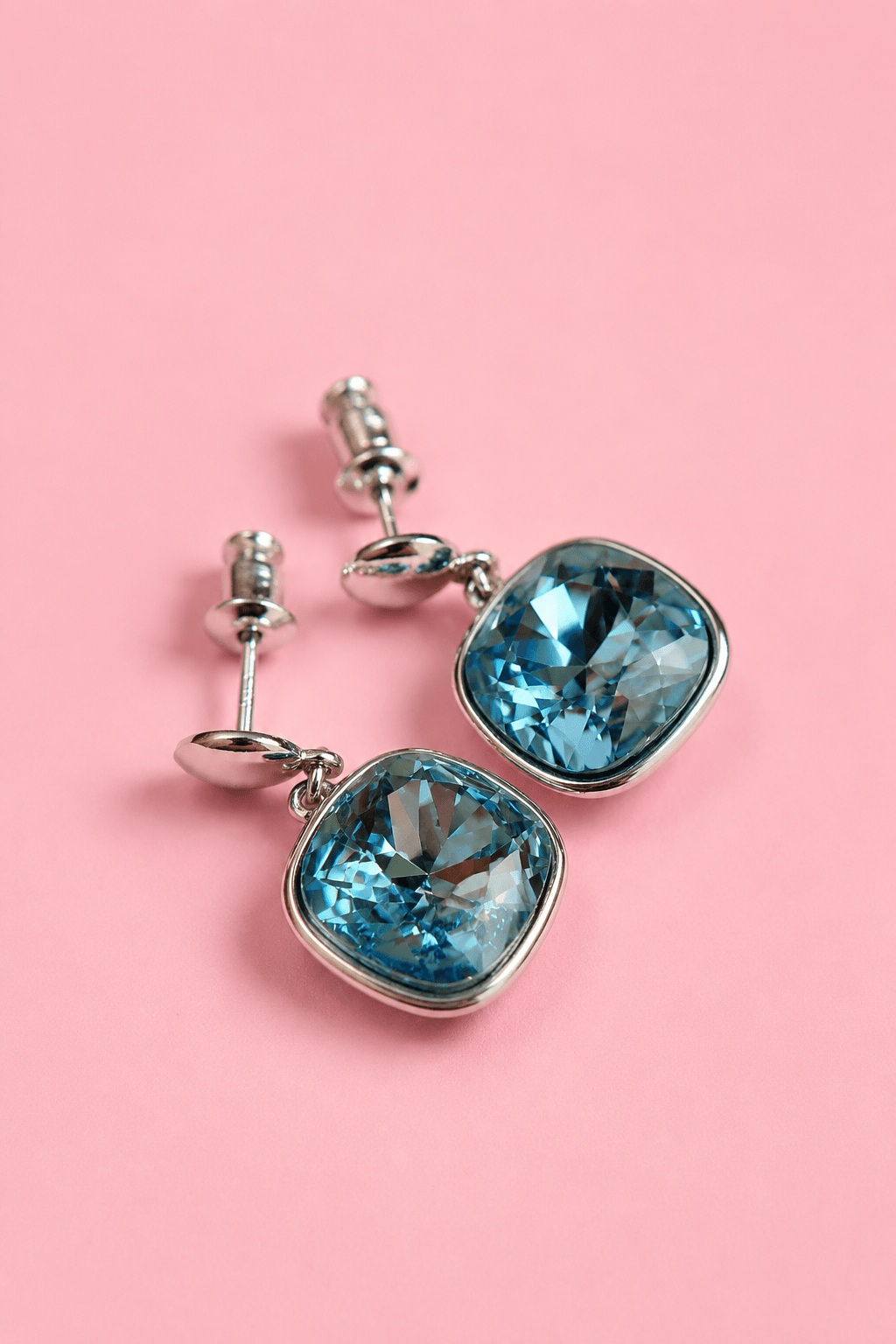 Silver plated stud earrings with aquamarine blue crystal on a pink background