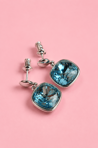 Silver plated stud earrings with aquamarine blue crystal on a pink background