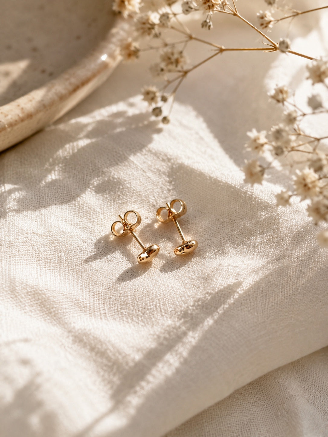 Sarah 18k gold-plated heart-shaped stud earrings on light fabric