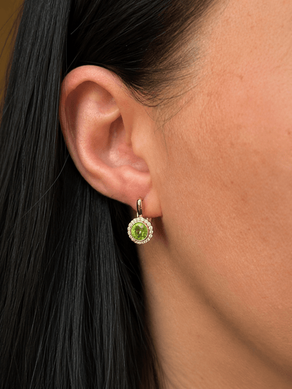 Gold-toned earring with a green center stone and clear rhinestones in the model's ear