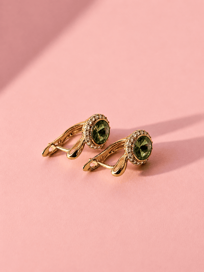 A pair of gold tone earrings with green center stones and English clasp on a pink background